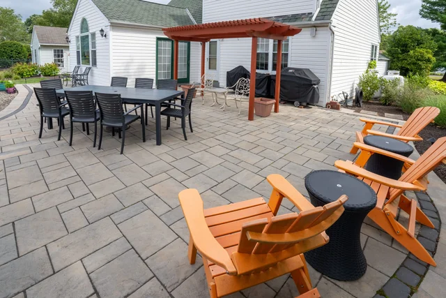 Blue Tree paver patio in Telford with a pergola, dining table and orange Adirondack chairs.