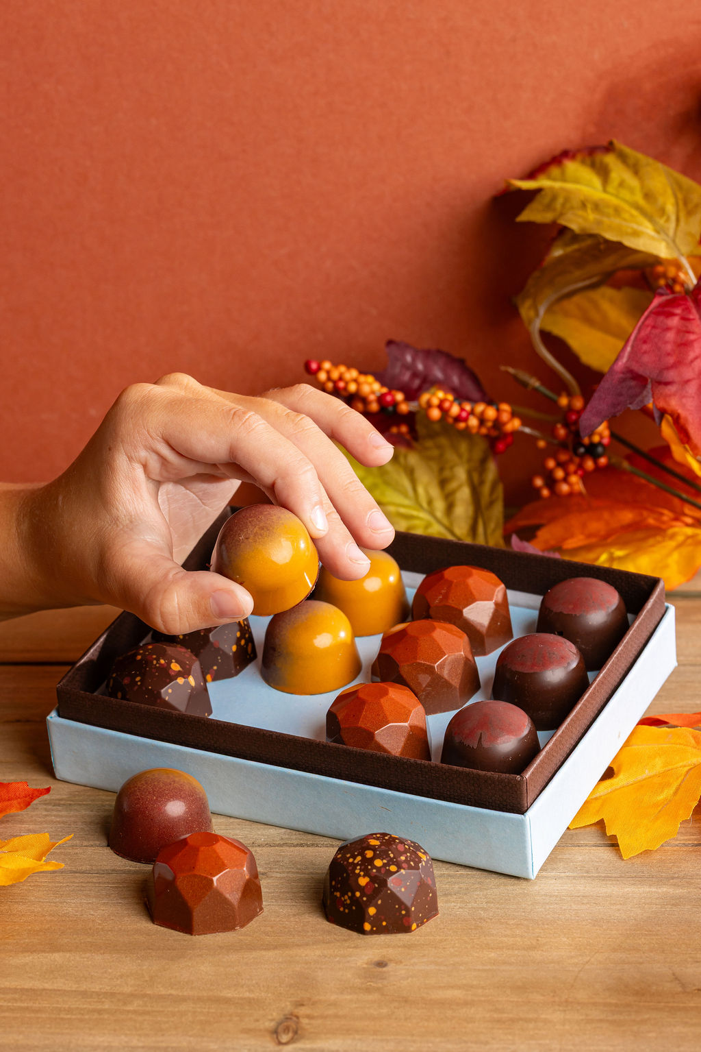 A hand lifts a caramel from an open little blue box of Fall Caramels