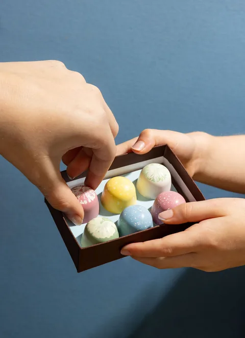 Hands sharing an open box of French Broad Chocolates bonbons. Product photography used in the new storefront.